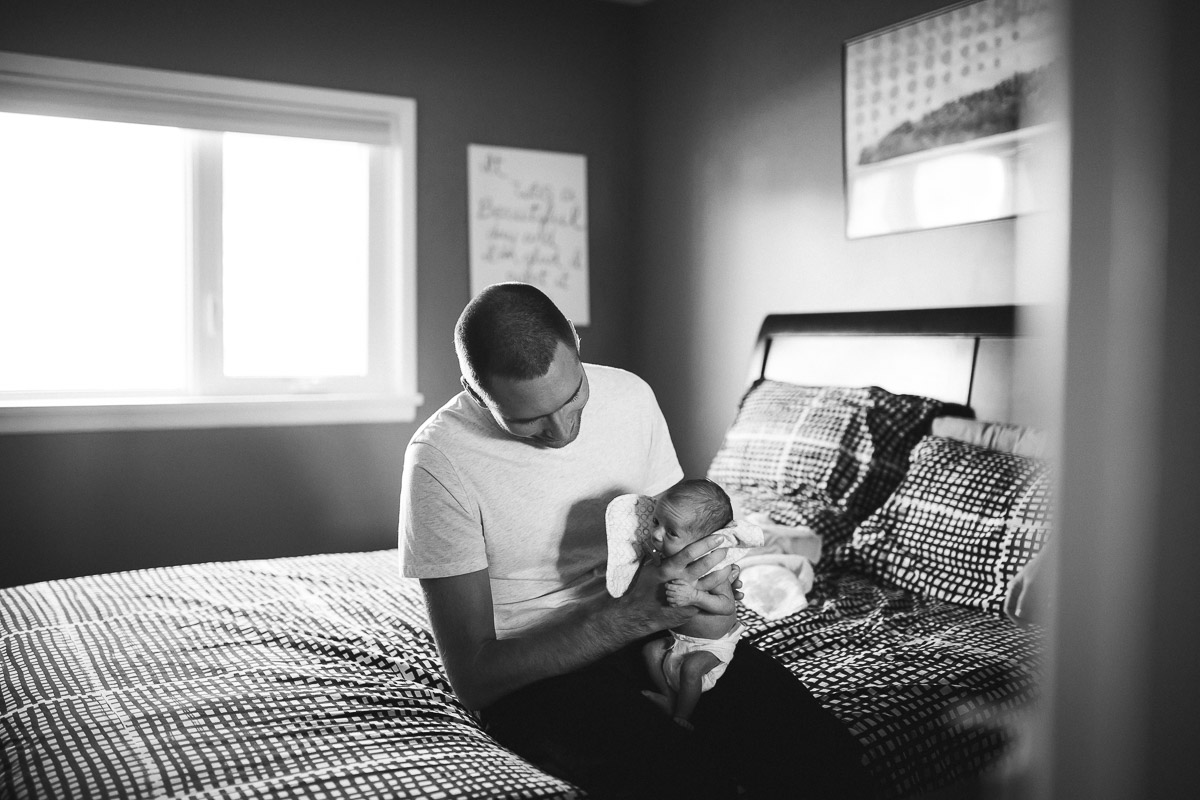 Dad sitting on bed burping his newborn baby girl. black and white