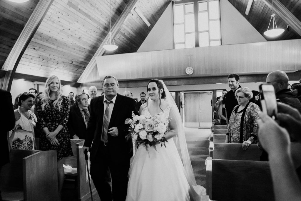 Bride and her dad walking down the aisle during Catholic Gimli wedding